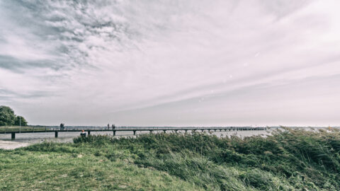 Bild: Blick vom Strand am Wieker Bodden auf die Seebrücke von Dranske auf der Insel Rügen. Foto: Copyright (c) 2020 by Birk Karsten Ecke. OLYMPUS OM-D EM-1 MkII mit M.ZUIKO DIGITAL ED 7‑14mm 1:2.8 PRO, ISO200, f/7.1, 1/500s, 7 mm. Klicken Sie auf das Bild um es zu vergrößern.
