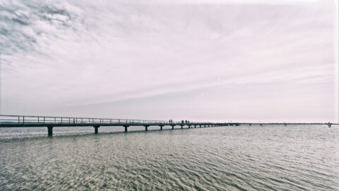 Bild: Blick vom Strand am Wieker Bodden auf die Seebrücke von Dranske auf der Insel Rügen. Foto: Copyright (c) 2020 by Birk Karsten Ecke. OLYMPUS OM-D EM-1 MkII mit M.ZUIKO DIGITAL ED 7‑14mm 1:2.8 PRO, ISO200, f/7.1, 1/1000s, 7 mm. Klicken Sie auf das Bild um es zu vergrößern.